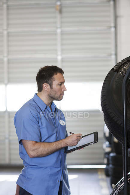 Mecânico masculino fazendo inventário de pneus novos na oficina de reparação de automóveis — Fotografia de Stock