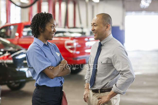 Male Pacific Islander auto repair shop manager talking to female Hispanic mechanic — Stock Photo