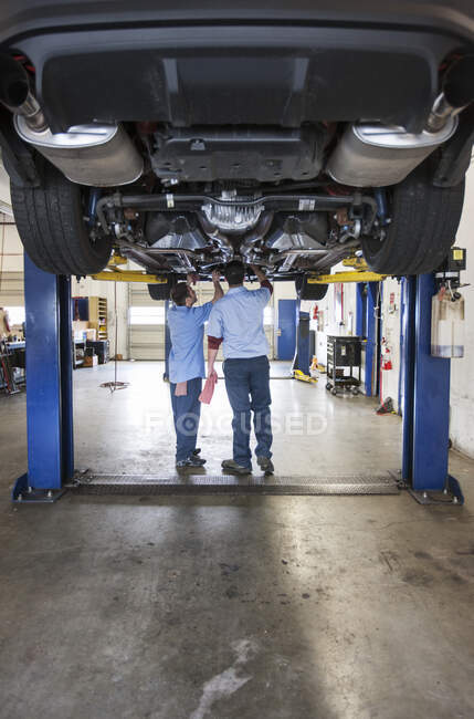 Zwei Mechaniker arbeiten an der Unterseite einer Hebebühne in einer Werkstatt — Stockfoto