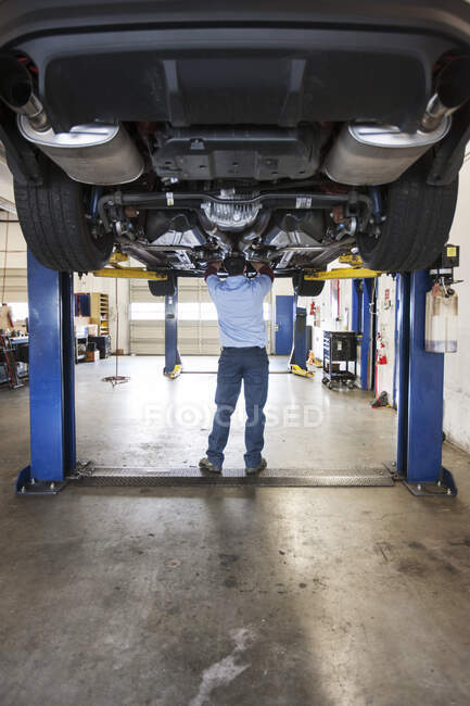 Mechaniker in einer Werkstatt bei der Arbeit an der Unterseite eines Autos auf einer Hebebühne — Stockfoto