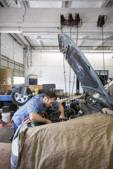 Mecánico en taller de reparación de automóviles se inclina en el motor del coche en el que trabaja - foto de stock