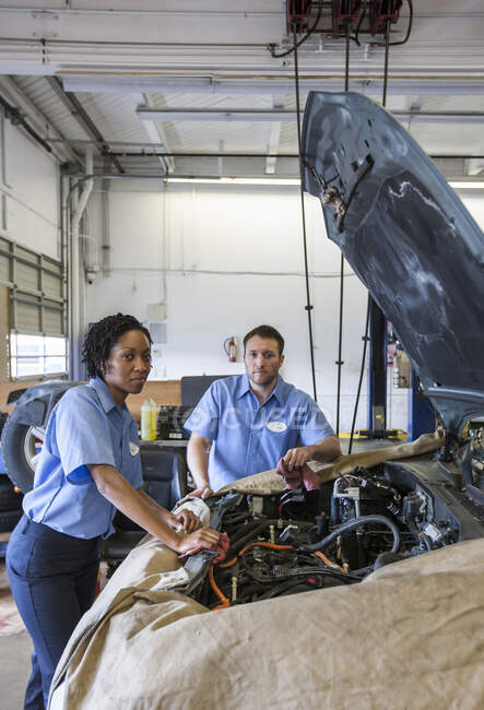 Männliche und weibliche Mechaniker unterhalten sich, während sie in der Autowerkstatt den Motor betrachten — Stockfoto