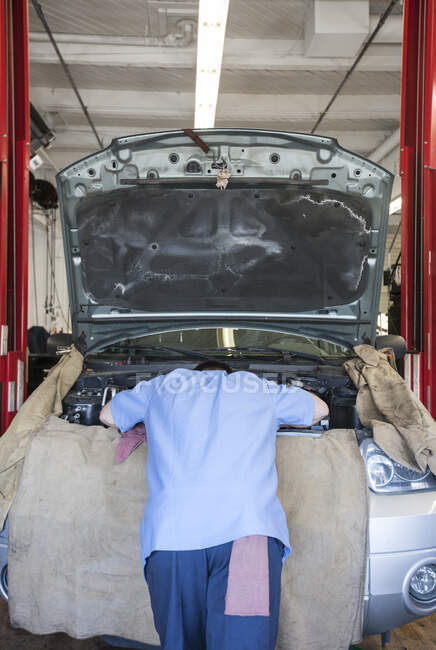 Torso de um mecânico inclinado para o compartimento do motor em uma oficina de reparação de automóveis — Fotografia de Stock