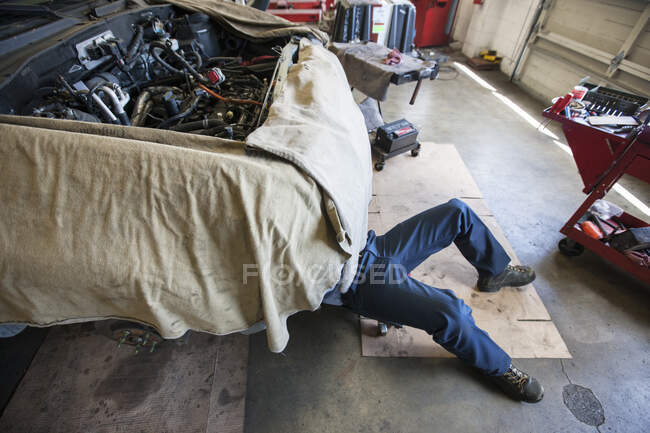 Mechaniker legt sich in einer Autowerkstatt auf einen Wagen unter ein Auto — Stockfoto