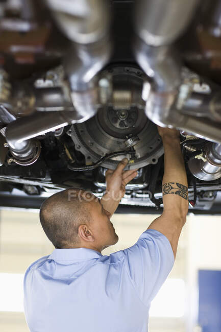 Pacific Islander mechanic works on the underside of a vehicle on a lift in an auto repair shop — Stock Photo