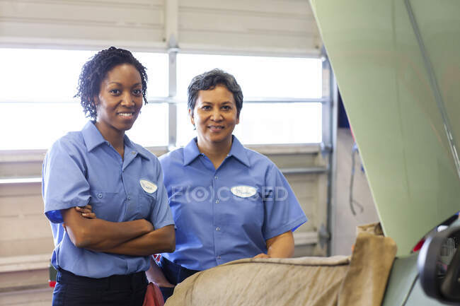 Retrato de dos mujeres mecánicas sonrientes en un taller de reparación de automóviles. - foto de stock