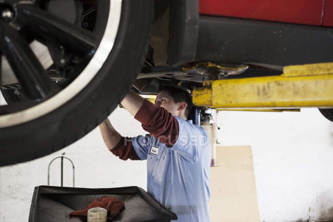 Mechaniker in einer Werkstatt bei der Arbeit an der Unterseite eines Autos auf einer Hebebühne — Stockfoto