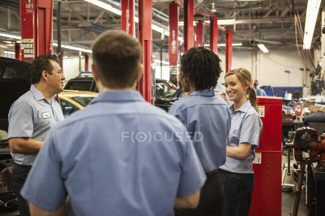 Team di meccanici che lavorano su un'auto discutono di un problema in un'officina di riparazione auto — Foto stock