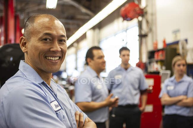 Portrait of smiling Pacific Islander repair shop owner with team in the background — Stock Photo