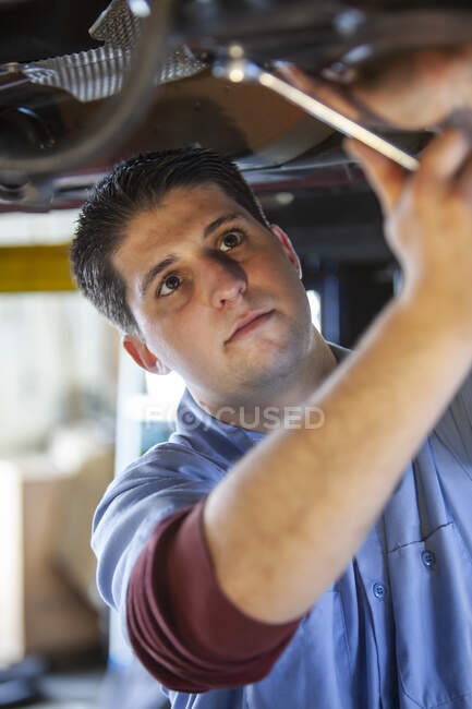 Meccanico in un'officina di riparazione che lavora sul lato inferiore di un'auto su un ascensore — Foto stock