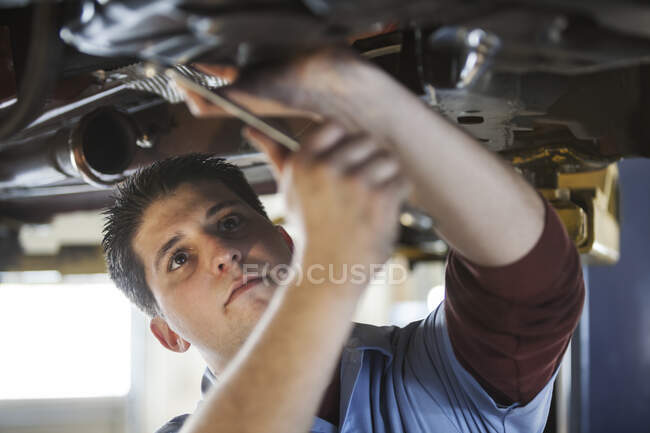 Mécanicien dans un atelier de réparation travaillant sur le dessous d'une voiture sur un ascenseur — Photo de stock