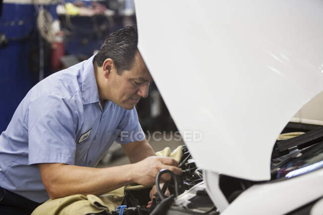 Hispanic mechanic leaning on a car working on the engine compartment in an auto repair shop — Stock Photo