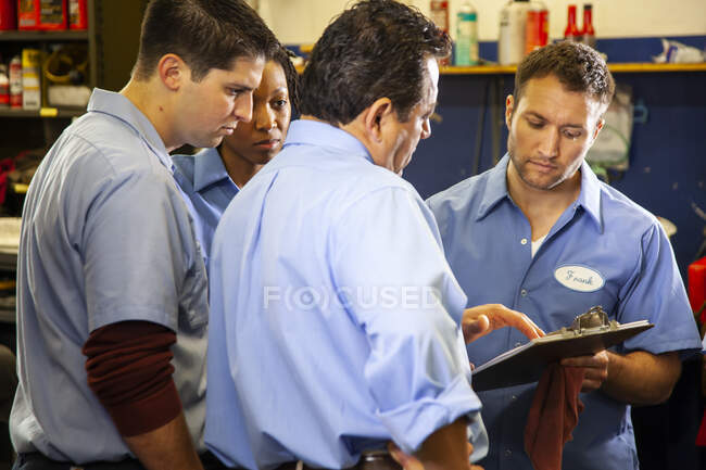 Équipe de mécaniciens travaillant sur une voiture discutant d'un problème dans un atelier de réparation automobile — Photo de stock