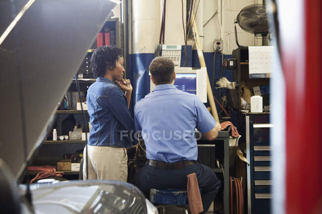 Механик и клиент смотрят на экран компьютера в авторемонтной мастерской — стоковое фото