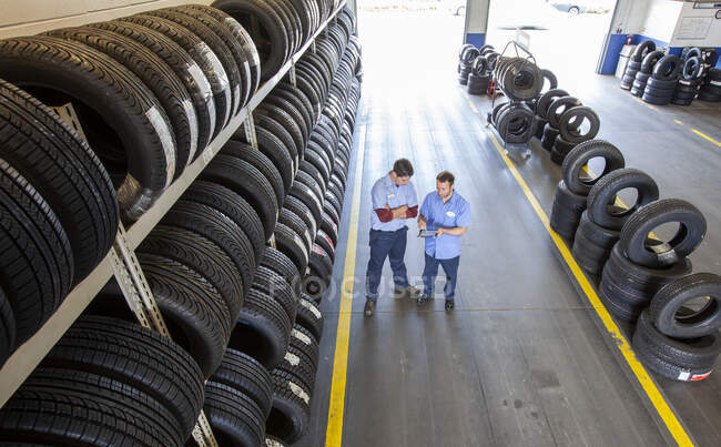 Due meccanici che lavorano nell'area pneumatici di un'officina di riparazione auto, utilizzando un tablet digitale — Foto stock