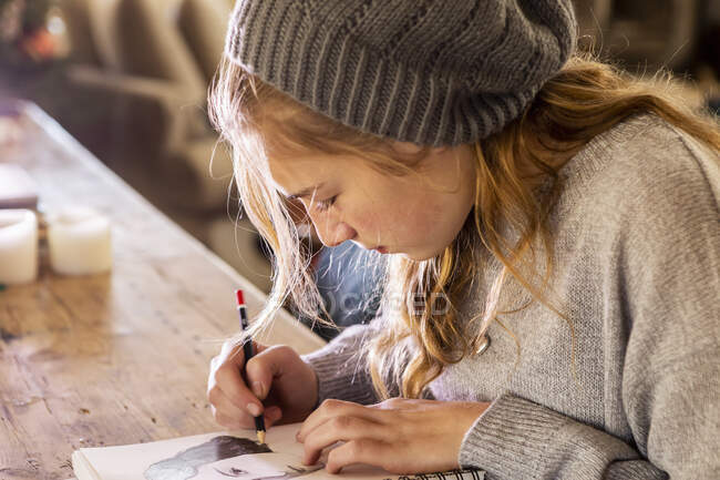 Adolescente em um chapéu de lã desenho com um lápis em um sketchpad. — Fotografia de Stock