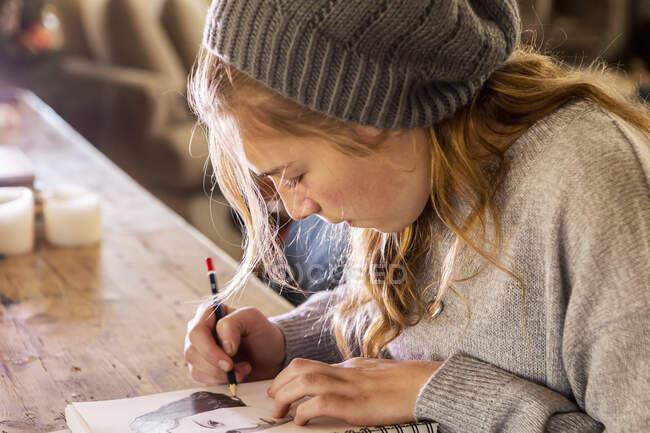 Adolescente em um chapéu de lã desenho com um lápis em um sketchpad. — Fotografia de Stock