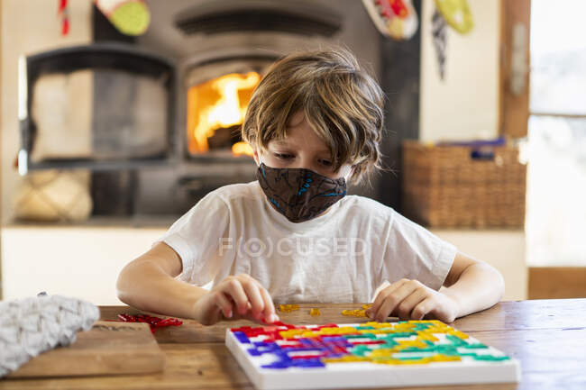 Joven niño usando máscara jugando juego de mesa en casa - foto de stock