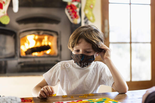 Giovane ragazzo indossando maschera gioco da tavolo a casa — Foto stock
