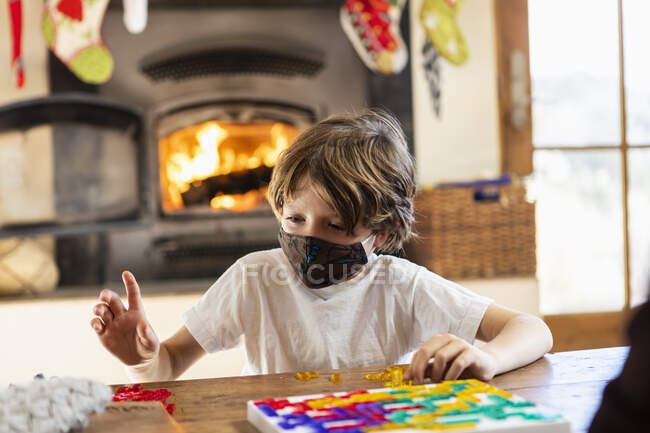 Junge mit Maske spielt Brettspiel zu Hause — Stockfoto