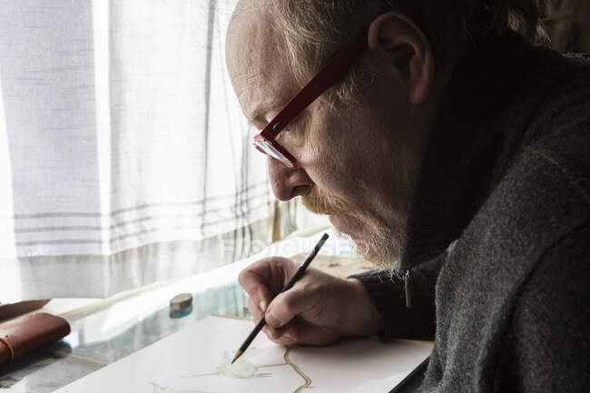 Artista maturo al lavoro disegnando su carta, uno studio della fauna selvatica degli uccelli. — Foto stock