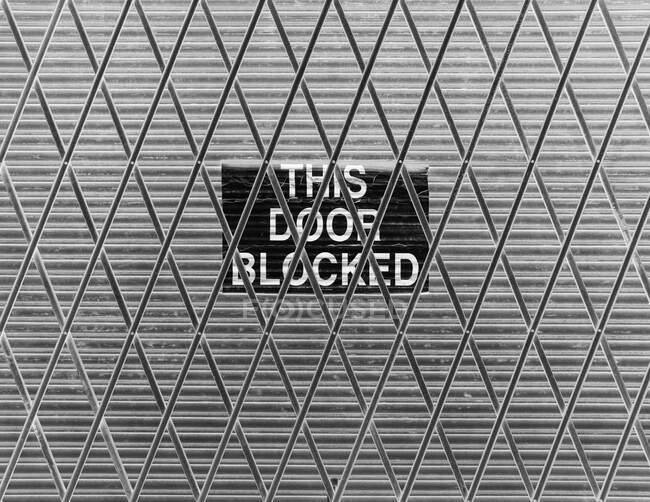 Metal grid fence with a sign saying This Door Blocked — Stock Photo