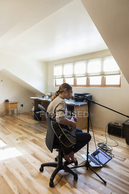 Четырнадцатилетняя девочка-подросток играет на гитаре и поет дома в мансарде — стоковое фото