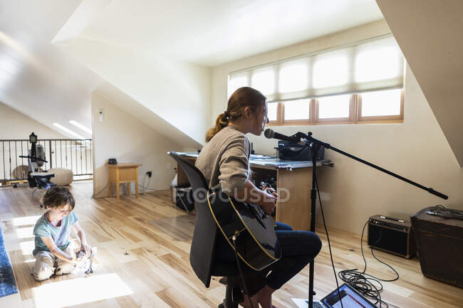 Fourteen year old teenage girl playing her guitar and singing, her brother playing in the background — Stock Photo