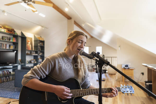 Adolescente de catorce años tocando su guitarra y cantando en casa en el loft - foto de stock