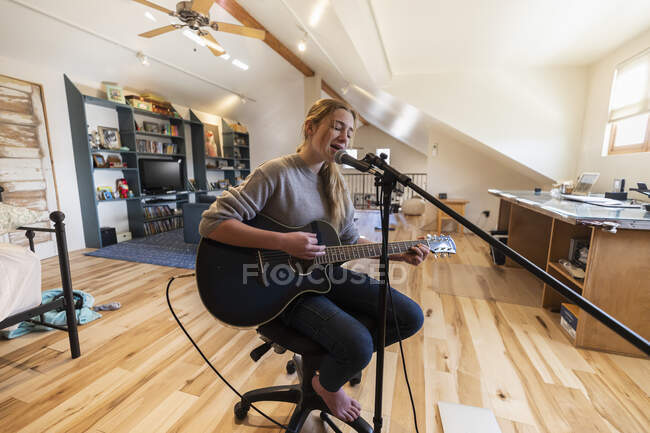 Adolescente de quatorze ans jouant de la guitare et chantant à la maison dans l'espace loft — Photo de stock