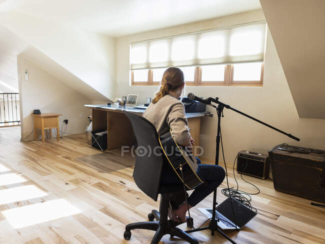 Fourteen year old teenage girl playing her guitar and singing at home in loft space — Stock Photo