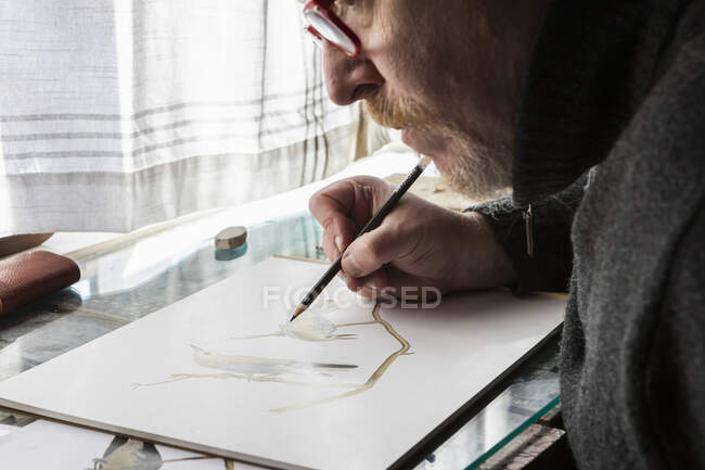 Зрелый художник за работой рисует на бумаге, изучает дикую природу птиц. — стоковое фото