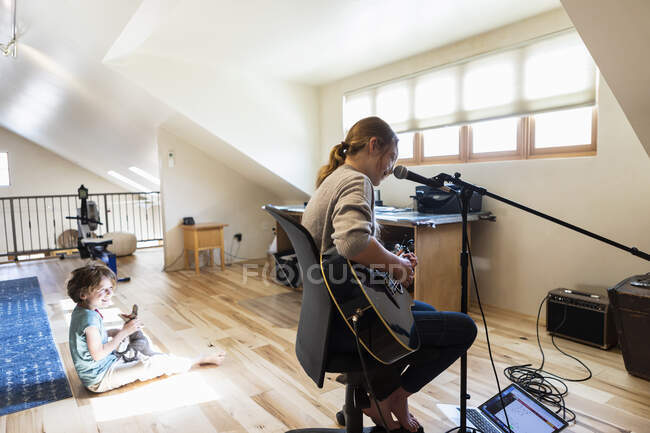Fourteen year old teenage girl playing her guitar and singing, her brother playing in the background — Stock Photo