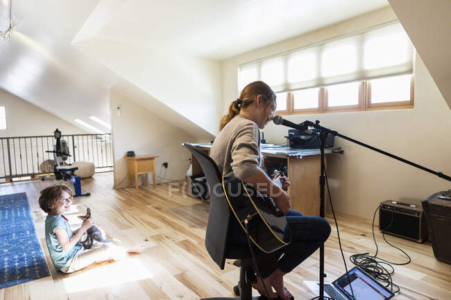 Четырнадцатилетняя девочка-подросток играет на гитаре и поет, ее брат играет на заднем плане — стоковое фото