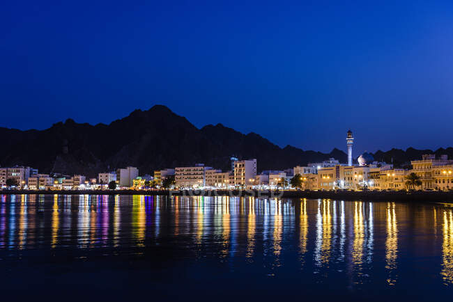A cidade de Mascate, luzes à beira-mar, montanhas atrás, à noite — Fotografia de Stock