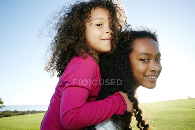 Young mixed race girl giving a younger sister a piggyback — Stock Photo