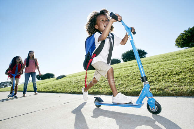 Niño de seis años en un scooter, seguido por su hermana - foto de stock