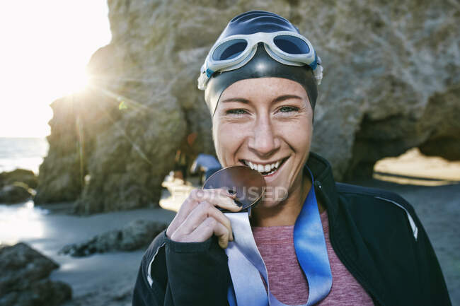 Junge Frau, Triathletin im Sakko, beißt mit den Zähnen auf eine große Medaille, eine Siegerin — Stockfoto