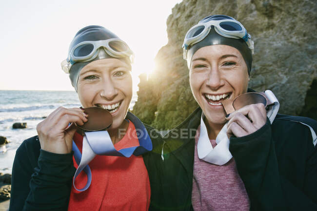 Due sorelle, triatleti che si allenano in costume da bagno, cappelli da bagno e occhiali che indossano le loro grandi medaglie, vincitori. — Foto stock