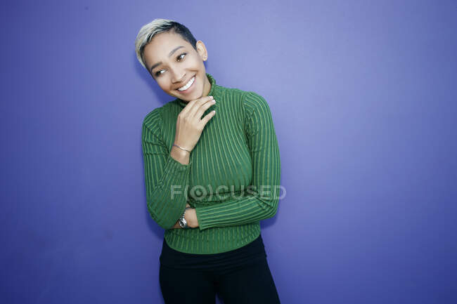 Jovem mulher negra sorrindo e olhando para o lado no fundo azul — Fotografia de Stock