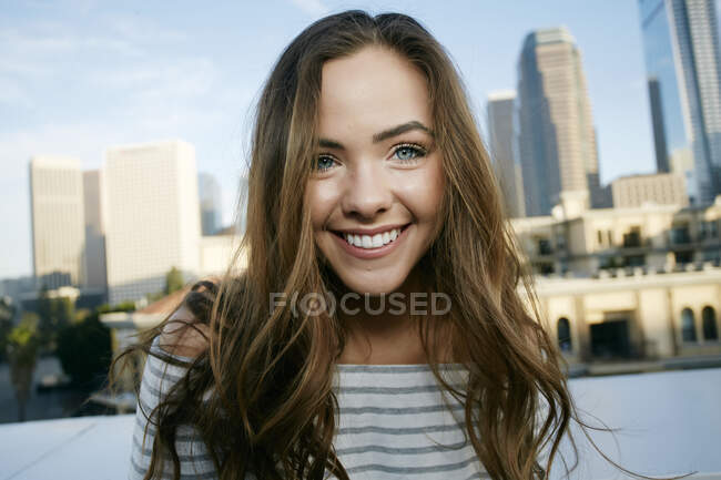 Portrait de jeune femme métissée sur un toit de ville souriant à la caméra, horizon derrière elle. — Photo de stock