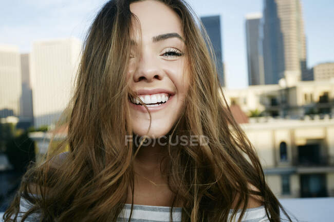 Retrato de una joven mestiza en un tejado de la ciudad sonriendo, horizonte detrás de ella. - foto de stock