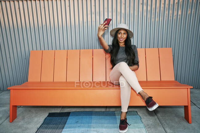 Giovane donna di razza mista in un cappello panama seduto a farsi un selfie, facendo una faccia — Foto stock