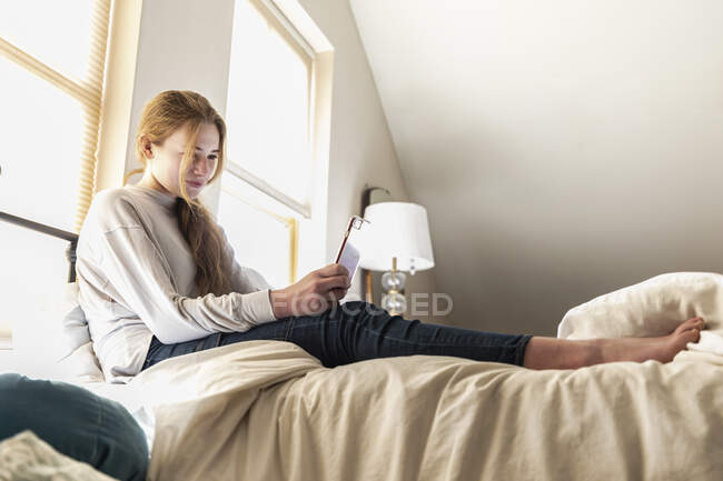Ragazza adolescente sdraiata a letto con il suo smart phone — Foto stock