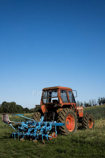 Tracteur rouge avec herse bleue sur une ferme. — Photo de stock