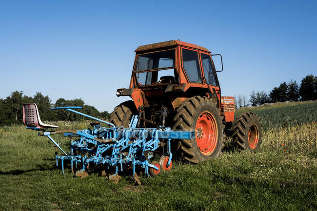 Roter Traktor mit blauer Egge auf einem Bauernhof. — Stockfoto