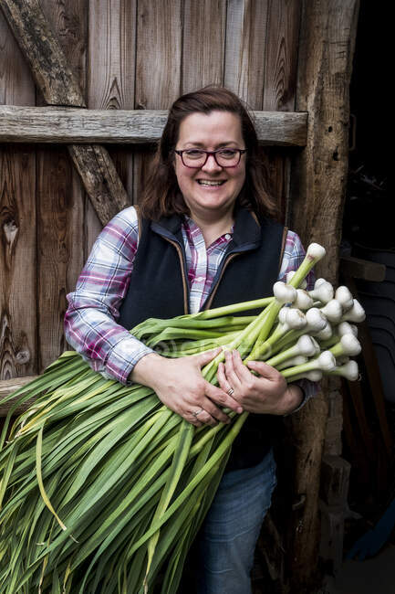 Smiling woman holding bunch of freshly picked garlic. — Stock Photo