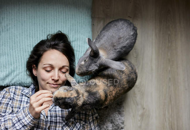 Woman lying on floor surrounded by two pet house rabbits shot from above —  smiling, Lying On Back - Stock Photo | #456280472