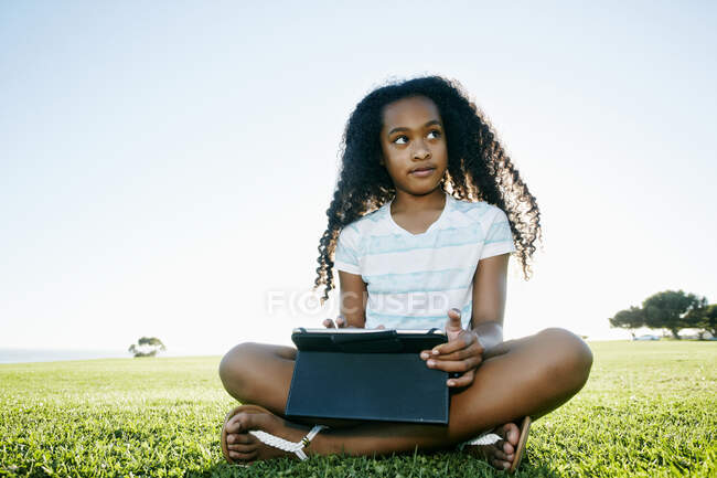 Девятилетняя девушка смешанной расы на открытом воздухе с цифровым планшетом. — стоковое фото