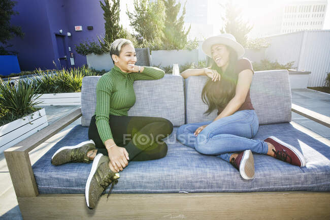 Duas jovens mulheres sentadas em um sofá em um jardim no telhado ao entardecer — Fotografia de Stock